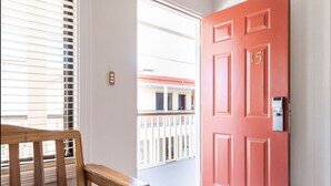 A red door with a keypad lock, a wooden bench, and a view of a balcony with a railing. - Prado Inn & Suites (San José)