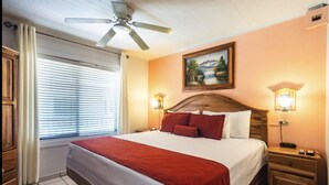 A hotel room with a bed, a ceiling fan, a painting on the wall, and two bedside lamps. - Prado Inn & Suites (San José)
