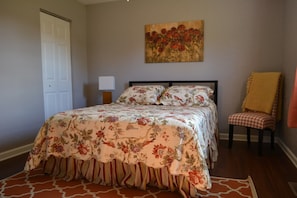Una camera da letto con un letto, una sedia, un quadro e una porta.