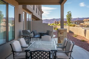 Une terrasse extérieure avec une table et des chaises, un barbecue et une vue sur les montagnes.