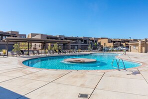 Une piscine avec un jacuzzi circulaire, entourée de chaises longues et d’un espace patio couvert.