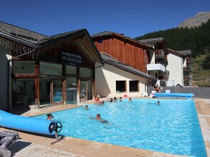 Ein Poolbereich mit einem hölzernen Gebäude mit der Aufschrift "Les Hauts de Préalux" und einem Berg im Hintergrund.