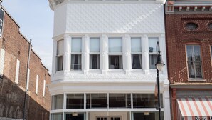 Un edificio blanco con techo de cúpula verde, ventanas amplias y un escaparate con toldo a rayas.