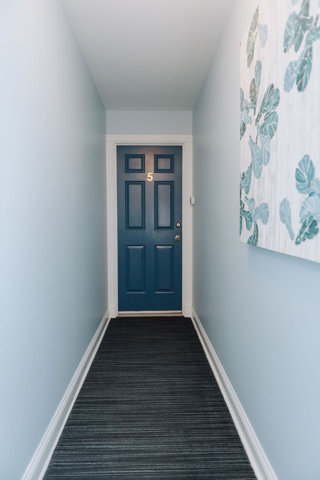 A hallway with a dark blue door marked with the number 5, leading to a room.