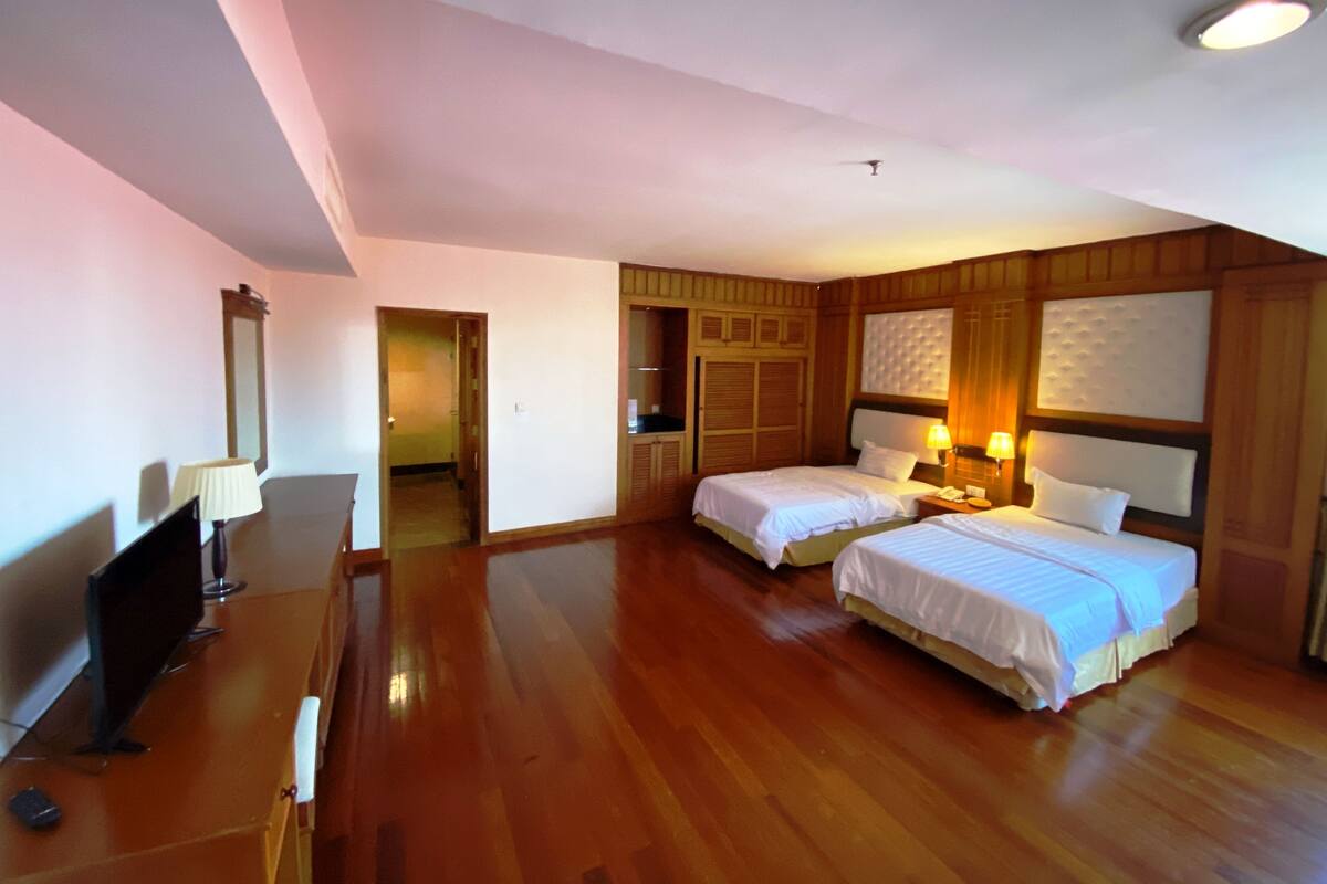 A hotel room with two beds, wooden flooring, a desk with a lamp, and a mirror.