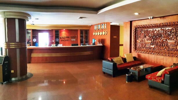 Vestíbulo de hotel con mostrador de recepción, sofás, una mesa de centro y un relieve decorativo en la pared.