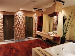 A modern bathroom with a stone wall, a wooden floor, a large mirror, a bathtub, and a vanity with a sink. - Oruseeey Hotel (Phnom Penh)