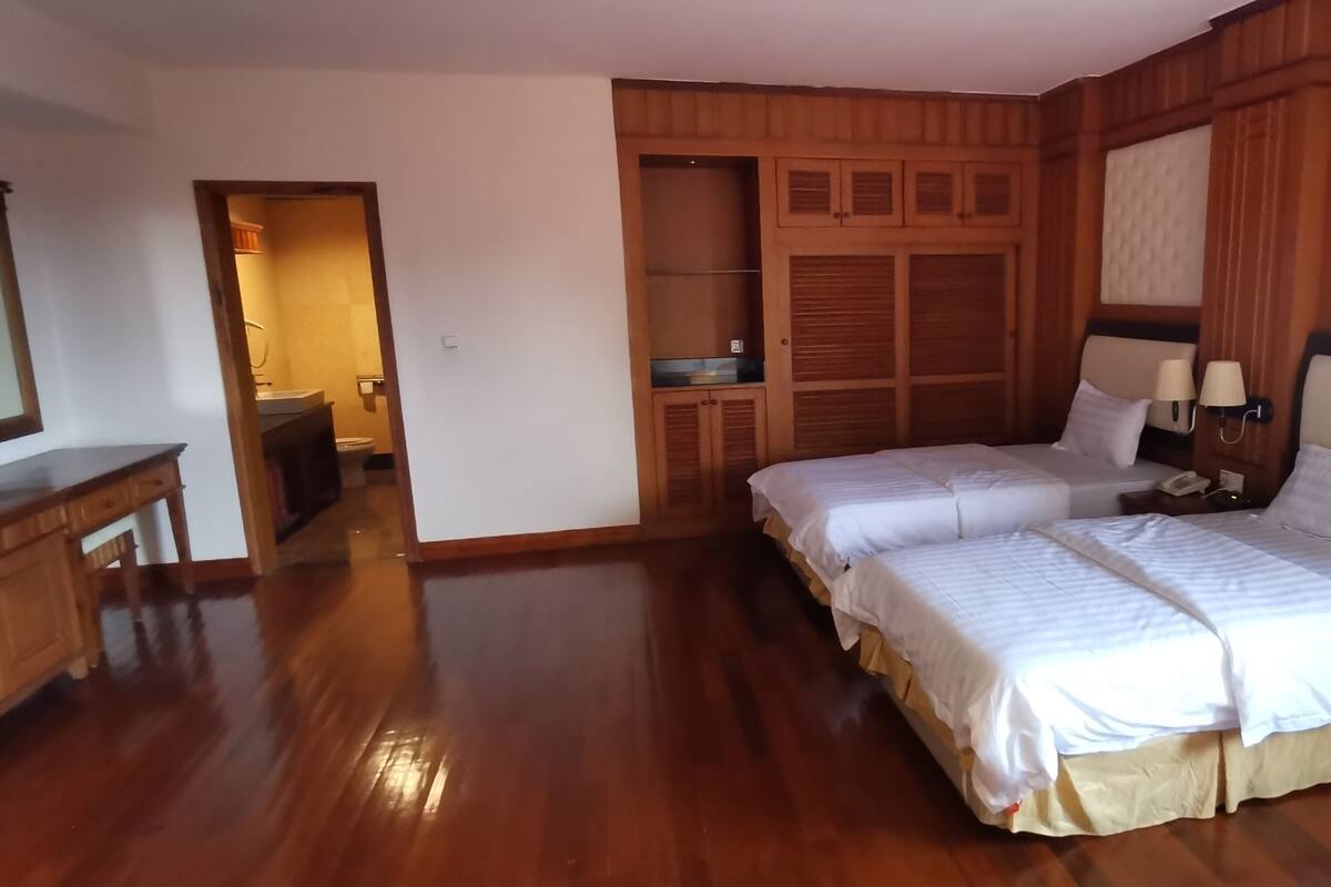 A hotel room with two beds, wooden paneling, a mirror, and a desk.