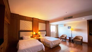 Habitación de hotel con dos camas, una zona de estar con una silla y una mesa, y una ventana con cortinas.