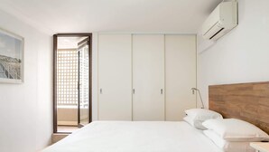 A bedroom with a bed, a nightstand, an air conditioning unit, and a door leading to a balcony. - Beachfront Manly Apartment With Balcony & Parking (Manly)