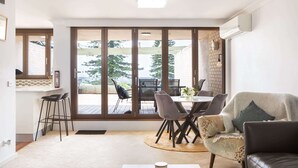 A spacious living area with a large sliding glass door leading to an outdoor patio. Inside, there is a dining table with chairs, a sofa, and a coffee table. - Beachfront Manly Apartment With Balcony & Parking (Manly)