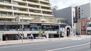 A modern building with multiple floors, a restaurant named 'Minato' on the ground floor, and a sign for 'Motel & Holiday Apartments' on the right. - Beachfront Manly Apartment With Balcony & Parking (Manly)