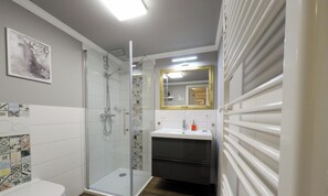 A bathroom with a shower, toilet, sink, and a mirror with a decorative frame.