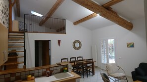 A spacious kitchen with a dining area, wooden beams, a staircase, and a view through a window.