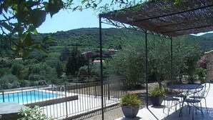 Ein Poolbereich mit umzäunter Terrasse, Sitzgelegenheiten im Freien und Blick auf eine hügelige Landschaft.