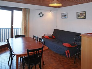 Ein Essbereich mit einem Holztisch und Stühlen, einer Couch mit roten Kissen, einer Uhr und zwei gerahmten Bildern an der Wand.
