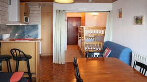 Um quarto aconchegante com uma mesa de jantar de madeira, duas cadeiras, uma cama beliche e uma cozinha compacta com micro-ondas.