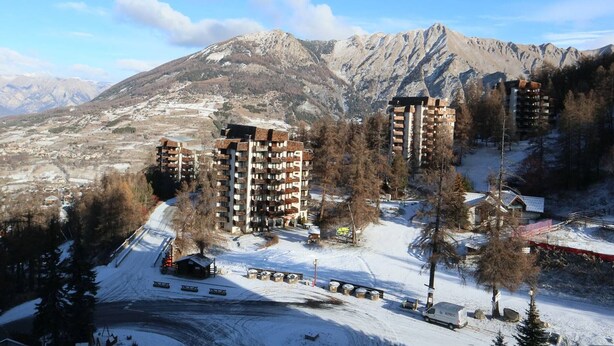 Uma região montanhosa com vários edifícios de vários andares, provavelmente hotéis, cercada por terreno e árvores cobertas de neve.