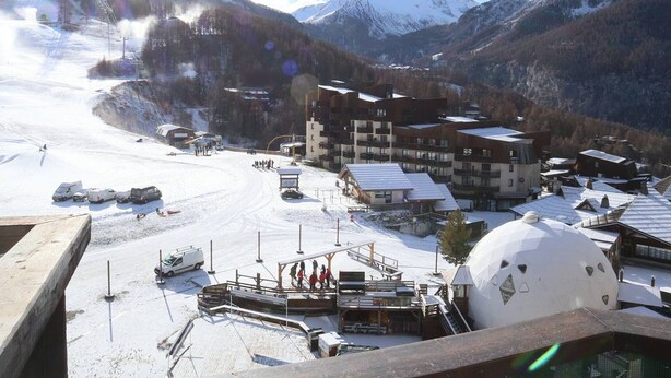 Ein Skigebiet mit einem großen Gebäudekomplex, einer schneebedeckten Piste und einer kuppelförmigen Struktur.