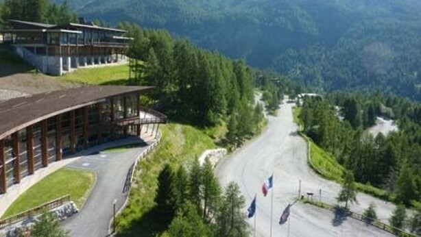 Un edificio moderno con techo curvo, rodeado de abundante vegetación y montañas al fondo.