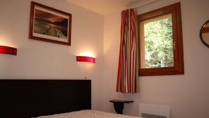 A bedroom with a bed, a framed picture on the wall, a window with curtains, and a bedside table.