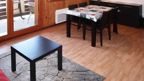 A dining area with a table and chairs, a television on the wall, and a view of the outside through a large window.