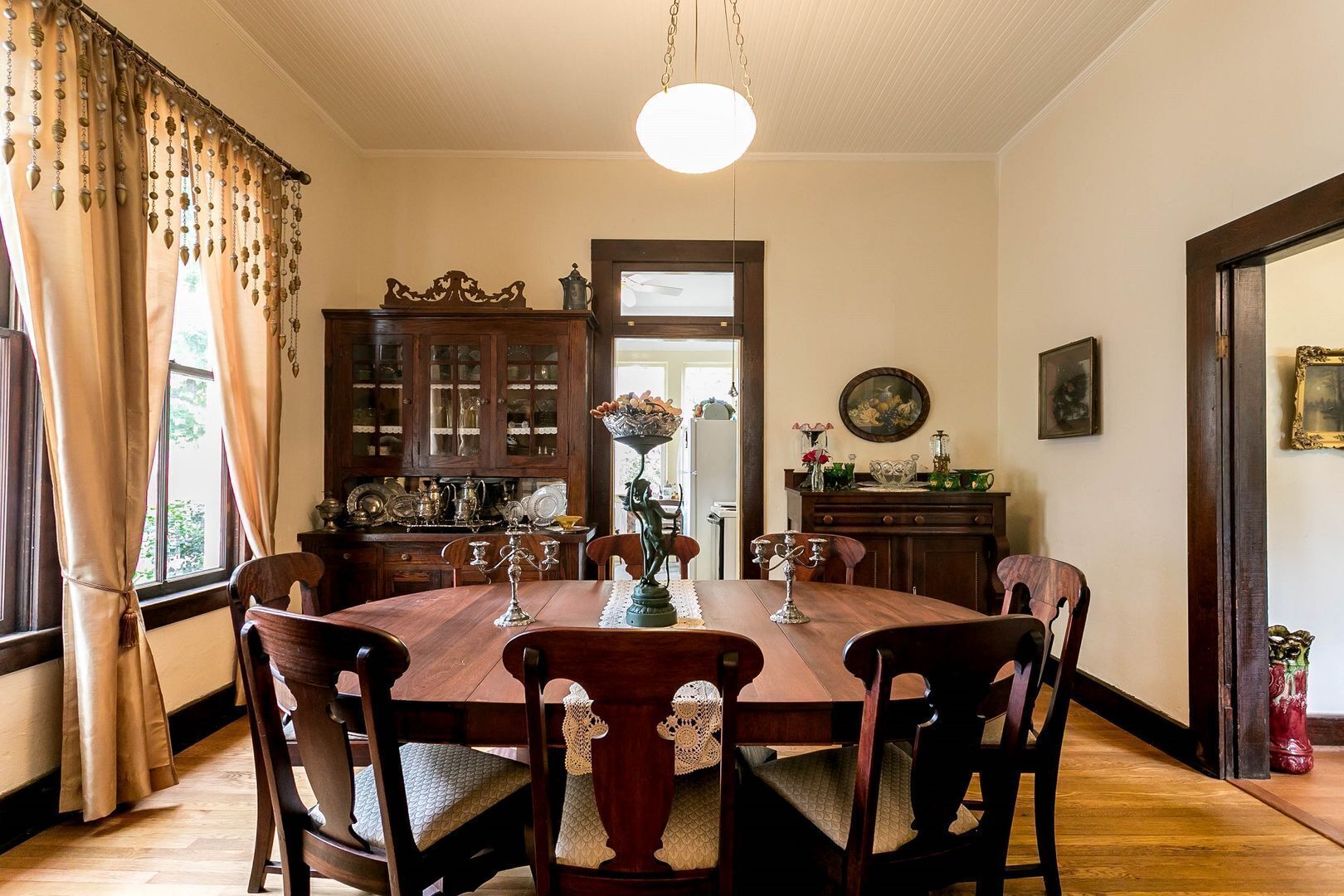 A dining room with a wooden table, chairs, and a chandelier. There are cabinets with glass doors and a painting on the wall.