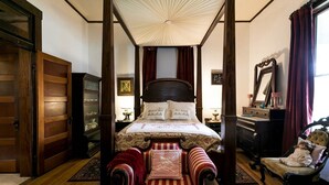 A four-poster canopy bed with a red and white striped chair in front, a wooden wardrobe, and a mirror on the right. - Alte Friedrichsburg | Historic Gem (Fredericksburg)