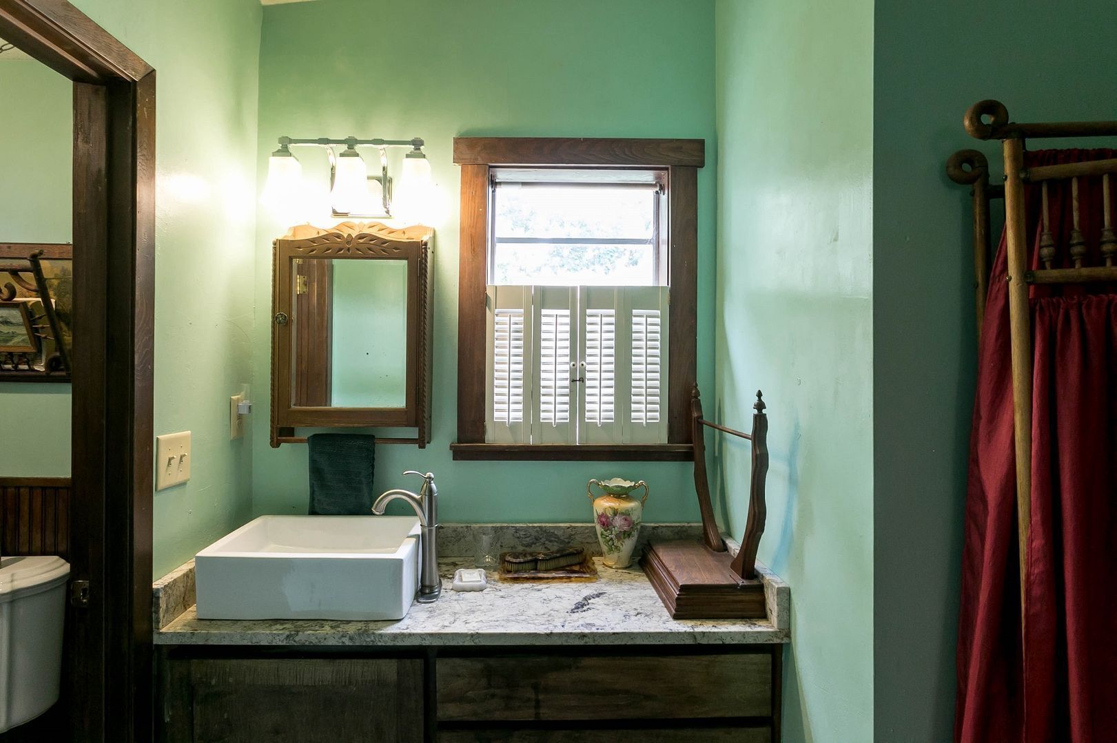A bathroom with a white sink, a mirror, and a window with shutters.
