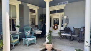 A porch with wicker furniture, a potted plant, and a sign reading "407 Cora". - Alte Friedrichsburg | Historic Gem (Fredericksburg)