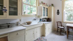 A kitchen with white cabinets, a sink, and a window with a view of trees. - Alte Friedrichsburg | Historic Gem (Fredericksburg)