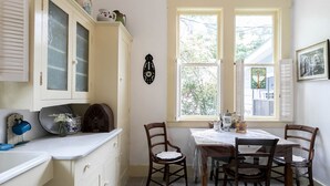 A kitchen with a dining table and chairs, a window with a view of trees, and a wall-mounted clock. - Alte Friedrichsburg | Historic Gem (Fredericksburg)