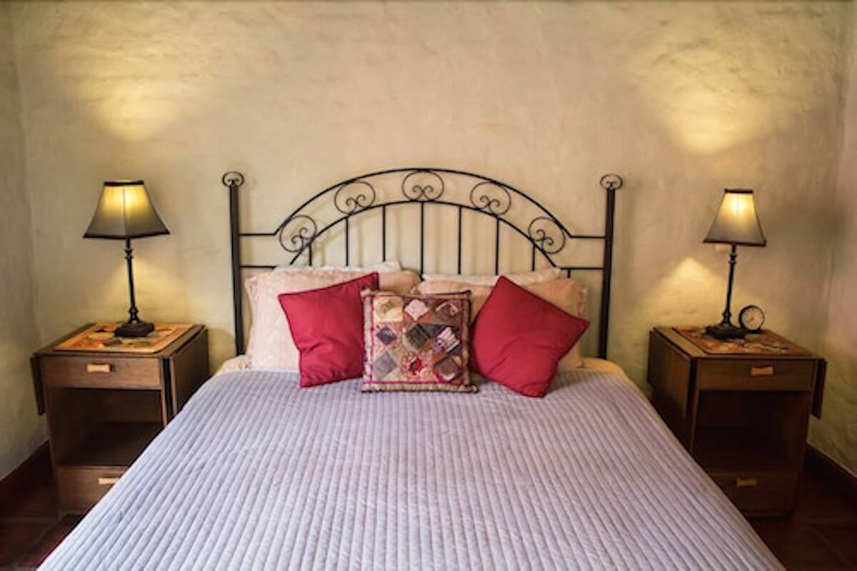 A neatly made bed with a striped bedspread and two red pillows, flanked by two bedside tables with lamps.