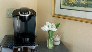Una cafetera sobre una encimera con un jarrón de flores blancas y un recipiente pequeño.