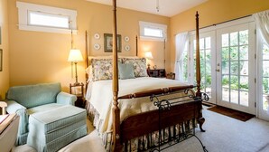 Una cama con dosel, un edredón floral, un sillón verde y una mesita de noche con una lámpara.
