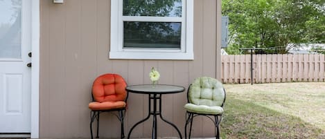 A porch with two chairs and a small table, a white door, and a window with blinds.