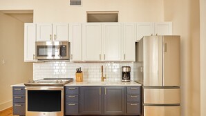 A modern kitchen with white cabinets, a stainless steel microwave, oven, and refrigerator, and a wooden countertop. - The Louie Hotel New Orleans, Belvilla District 6 Formerly Sonder (New Orleans)