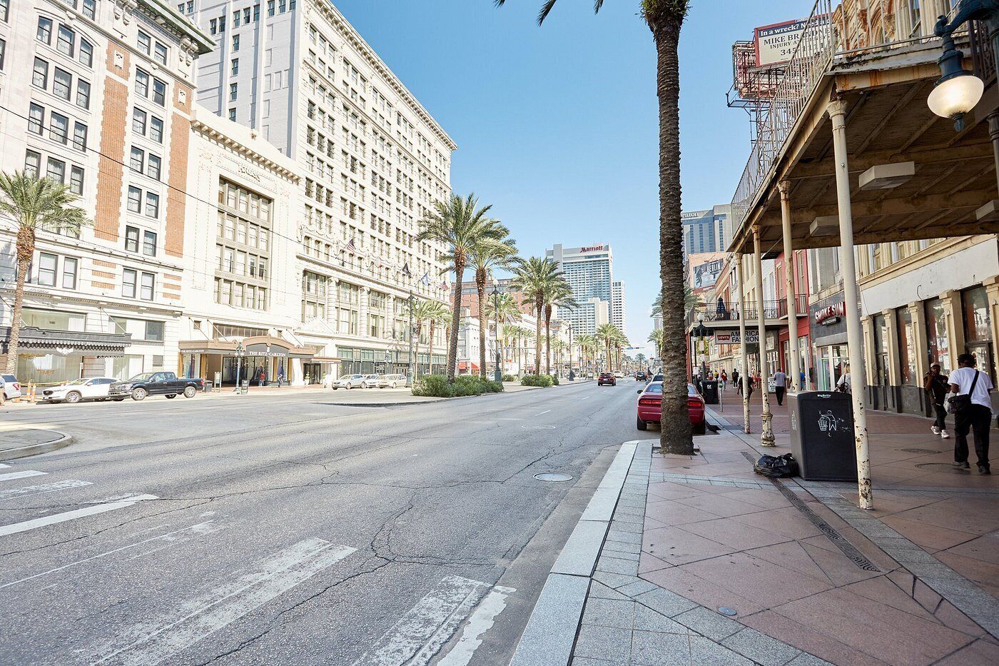 A street view with a hotel on the left, palm trees, and a clear sky.