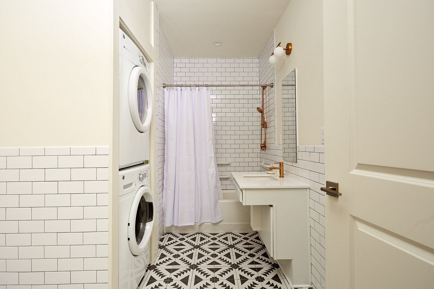 Un baño pequeño con lavadora, ducha con cortina, lavabo con espejo y baldosas de suelo estampadas.