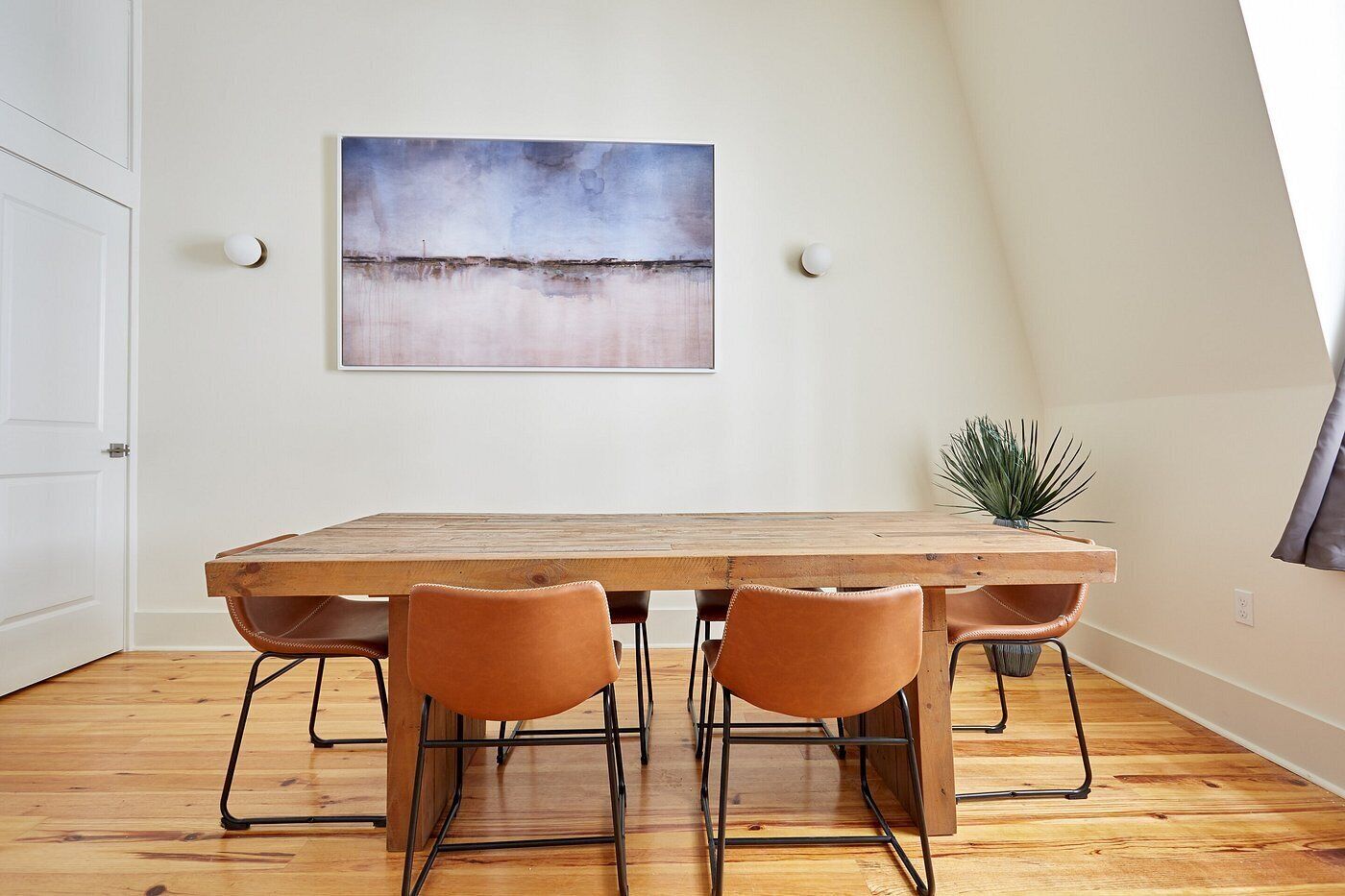 Ein Essbereich mit Holztisch, vier Stühlen, einem Bild an der Wand und einer Pflanze auf dem Boden.