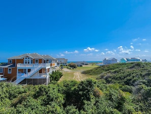 Um imóvel à beira-mar com uma casa de vários andares, uma escadaria visível e um caminho que leva à praia.