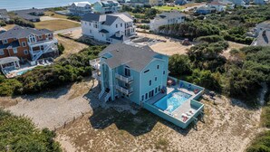 Ein großes, zweistöckiges Haus mit Swimmingpool, umgeben von weiteren Häusern und einem Strand.