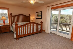 A bedroom with a wooden bed, a nightstand, a lamp, a painting, and a sliding glass door to a balcony. - Aqua Vista - Beautiful 7 BR, 6.5 BA, Oceanside w/ Private Pool (Southern Shores)
