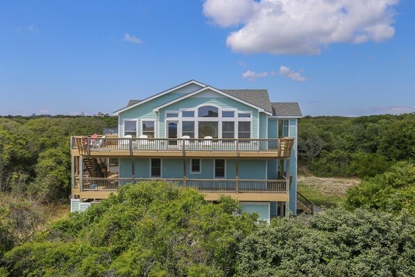 A two-story house with a balcony on the upper level, surrounded by dense vegetation. - Aqua Vista - Beautiful 7 BR, 6.5 BA, Oceanside w/ Private Pool (Southern Shores)