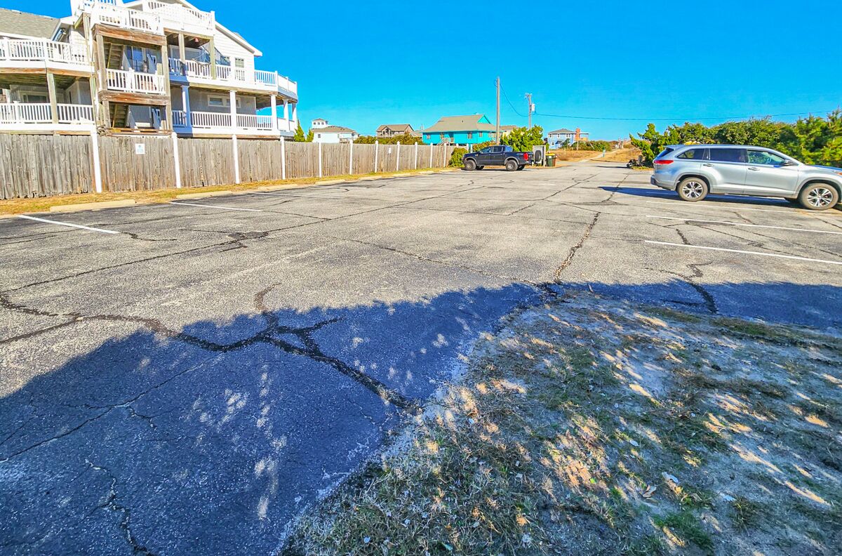A parking lot with a damaged asphalt surface, a wooden fence, and a building with balconies.