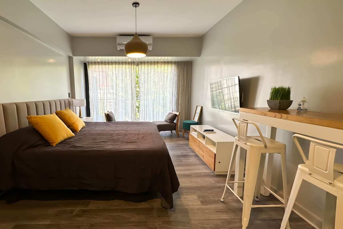Un dormitorio moderno con una cama grande, un escritorio con silla, un televisor y una ventana con cortinas.