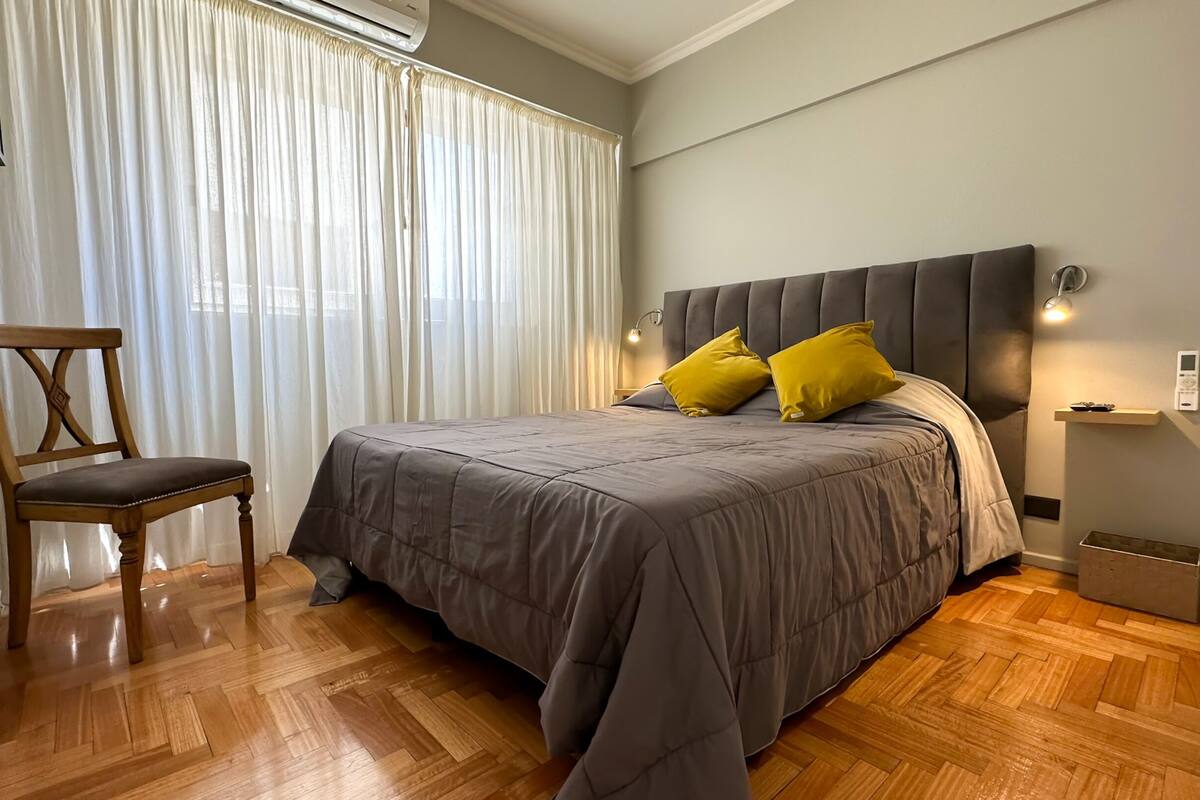 Un dormitorio con cama, una silla, una mesita de noche y una mesita auxiliar.