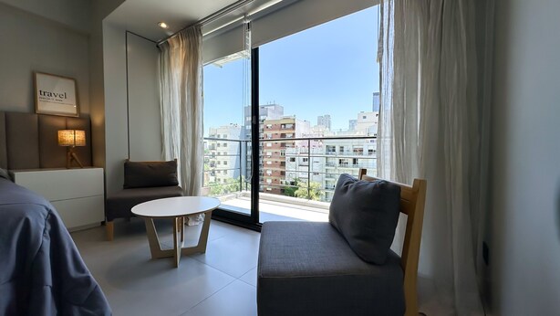 A modern hotel room with a large window, a sofa, a small table, and a lamp. - Soho Rentals (Buenos Aires)