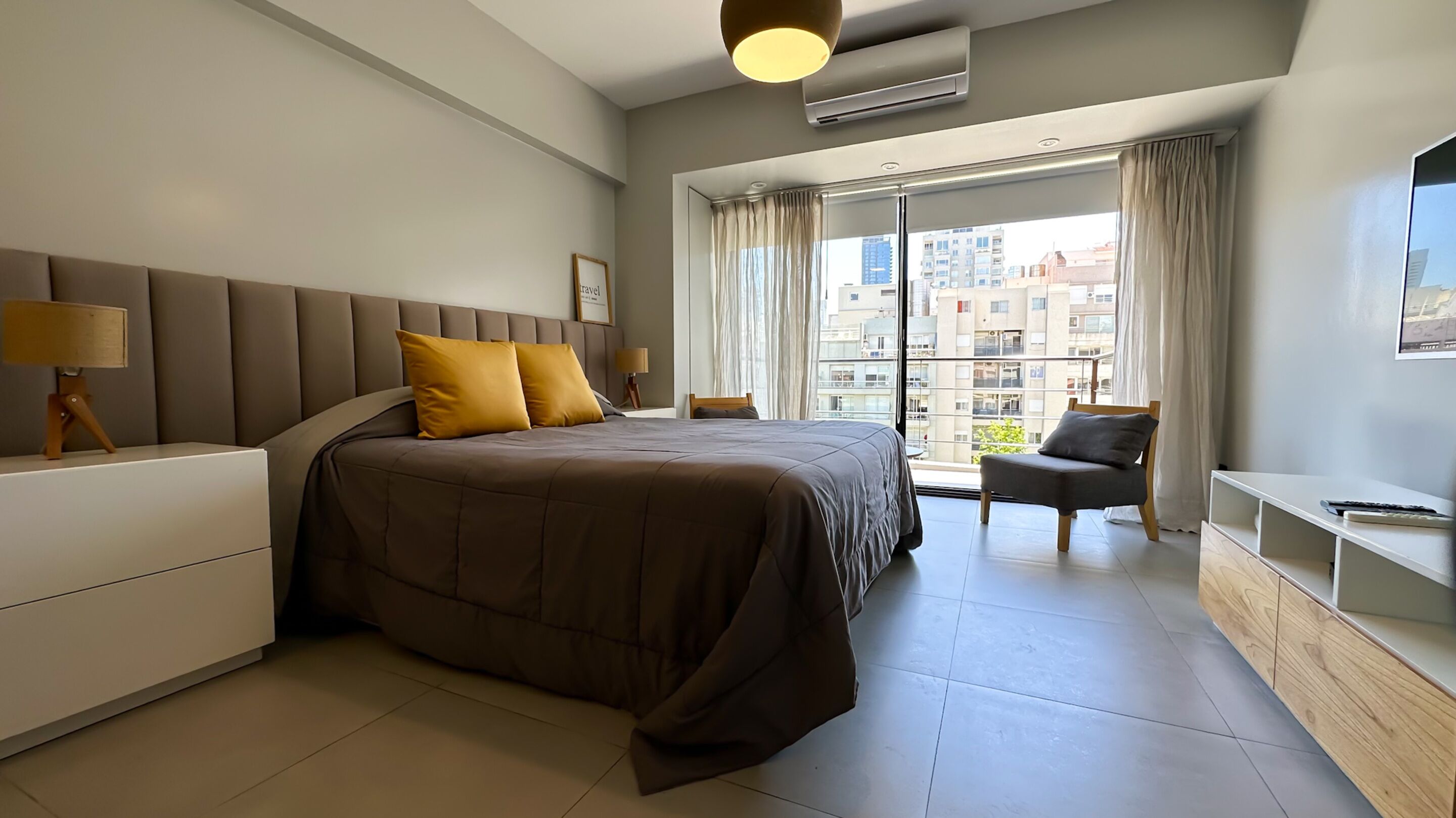 Habitación de hotel moderna con una cama grande, un escritorio, una silla y vistas de la ciudad a través de amplios ventanales.