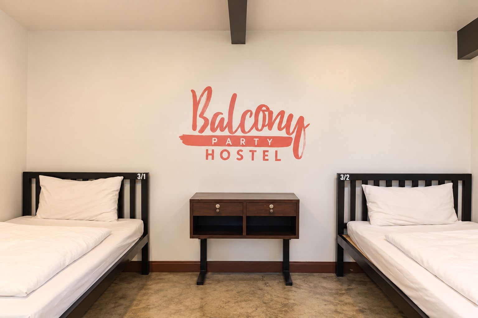 A bedroom with two beds, a nightstand, and a wall sign that reads 'Balcony Party Hostel.'